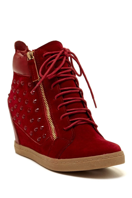 Red wedge sneakers with a textile upper, side zipper, and studded detailing, featuring a 3” heel and rubber outsole.